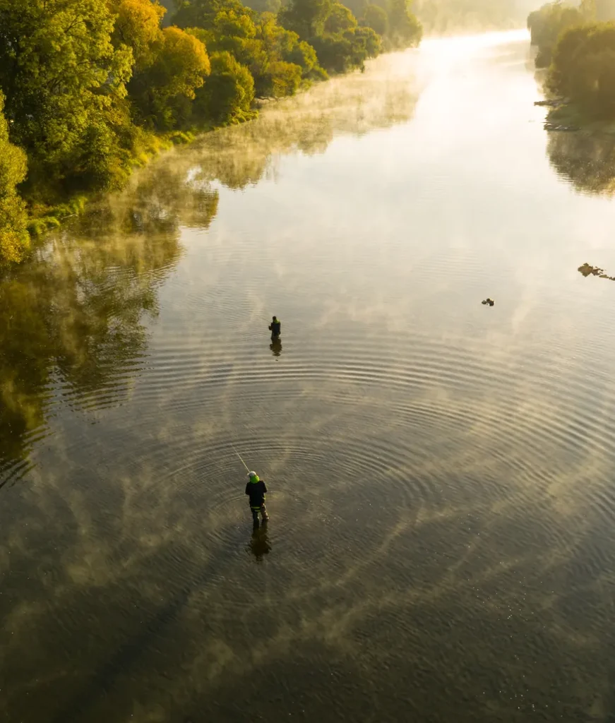 Aerial view of anglers fly fishing a calm river at sunrise